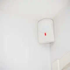 Detector de presencia blanco en esquina de pared, con luz roja encendida. Así es como funciona un detector de presencia.