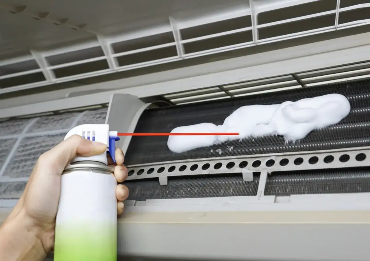 Mano rociando espuma para limpiar aire acondicionado.