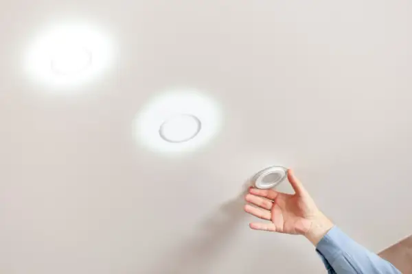 Mano instalando una lámpara techo redonda. Dos luces circulares ya iluminan el techo blanco.