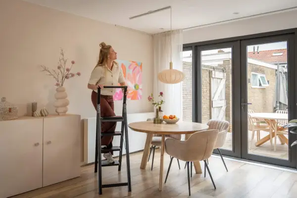 Mujer en escalera ajustando una lámpara colgante de dos luces sobre una mesa de comedor.